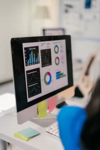 Focused businesswoman analyzes Account Based Marketing Analytics on her computer, using graphs to plan for growth. Her cluttered desk shows her dedication to success